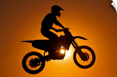 Silhouette of motocross race in mid air at sunset.