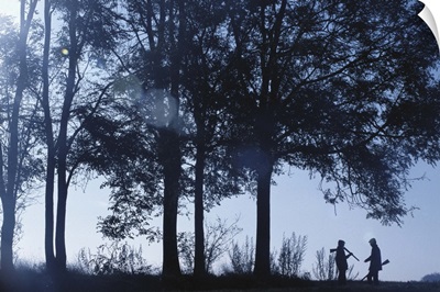 Silhouette of two men standing with shotgun in forest