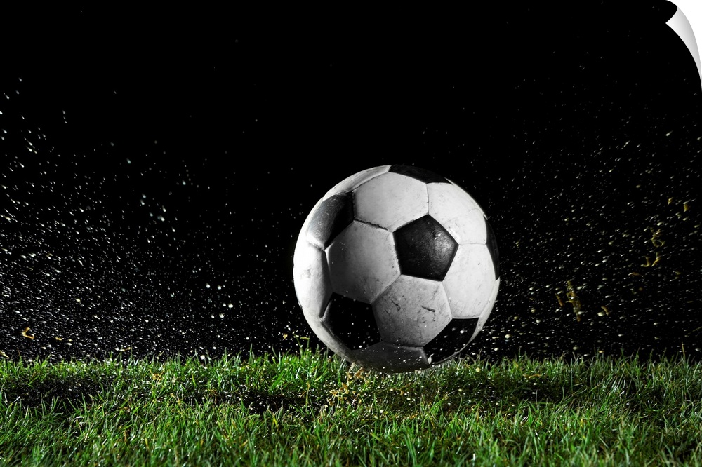 Photographic print of a soccer ball moving across wet grass from a kick.