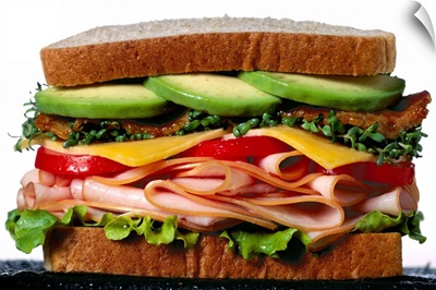 Stacked turkey sandwich with avocados, cheese, tomatoes and crunchy lettuce