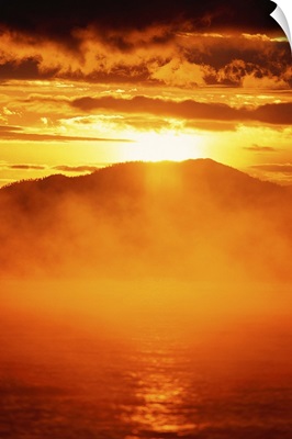 Sunset view of mist rising from lake, mountains in background