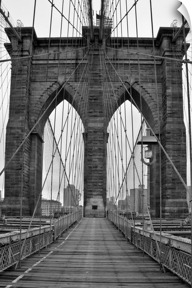 Large, vertical black and white photograph of one of the stone piers surrounded by many cables on the Brooklyn Bridge in N...