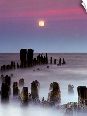 The full moon rises over Lake Michigan as rolling waves wash over the remnant of a pier.