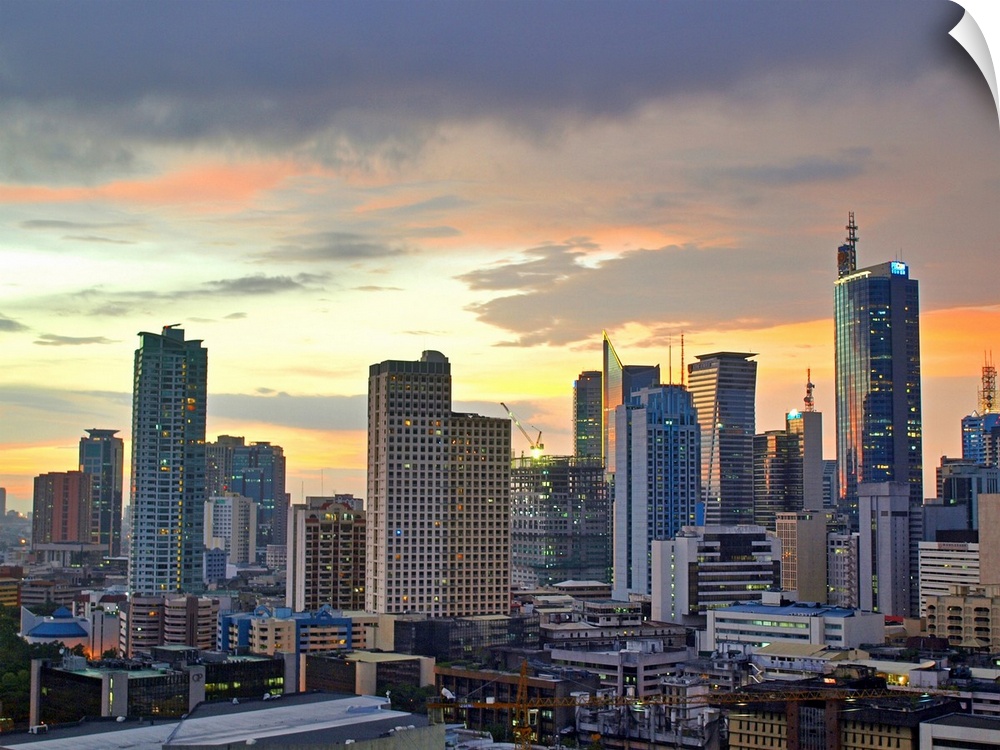 The sun setting light up low clouds over the Makati City, Manila Skyline. Many Tall buildings and a crane are seen with th...