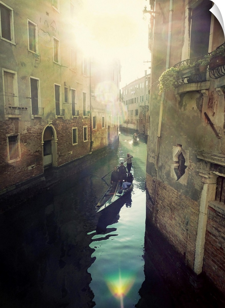 Portrait, oversized photograph of two gondolas floating toward the bright sun, through a canal in Italy, with tall buildin...