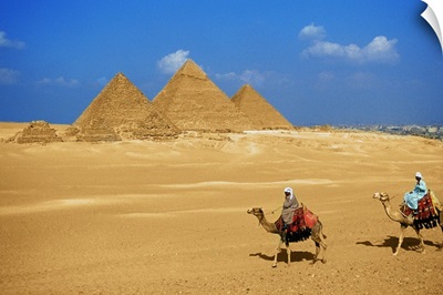 Two people riding camels near the pyramids of Giza, Egypt