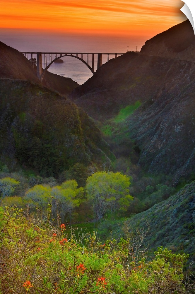Portrait oriented photo of the Big Sur bridge at sunset with rolling hills in the foreground and ocean in the background.