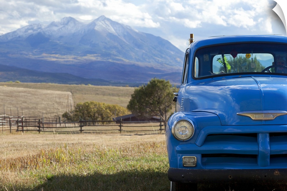 Landscape, large photograph of part of the front of a blue, vintage truck, parked in a grassy field, surrounded by vast fa...