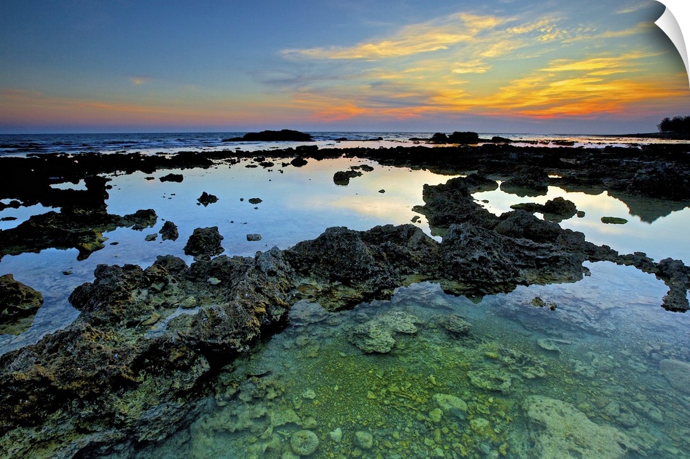Coral reefs in Wanliton at blue dusk with crystal clear water surrounded and orange clouds above  horizon.
