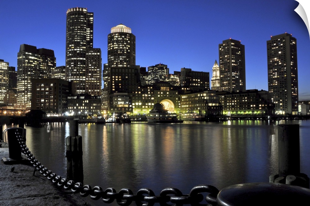 Downtown Boston and Financial District skyline lit up against a deep blue, late twilight sky, with lights reflected in Bos...