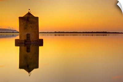 Windmill at sunset in middle of water and reflection in water.