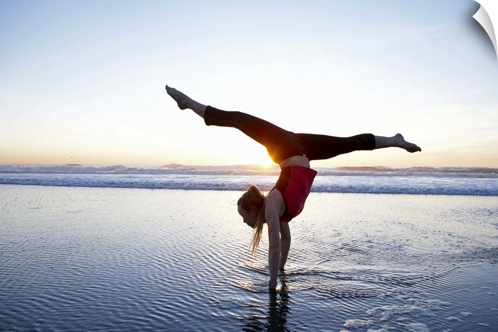 Woman doing a hand-stand on the beach at sunset.