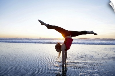 Woman doing a hand-stand on the beach at sunset