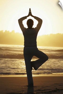 Woman doing yoga on beach at sunrise