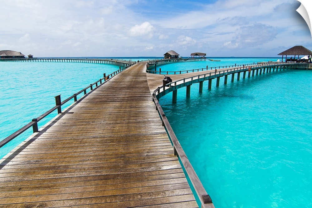 This wide angle landscape photograph shows a tropical destination of small huts and gazebos accessible by a pier over the ...