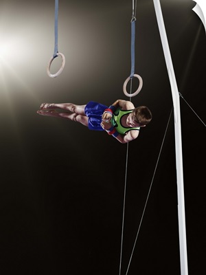 Young male gymnast dismounting from rings