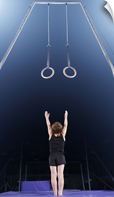 Young male gymnast reaching up to rings