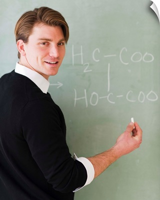Young teacher writing equation on blackboard