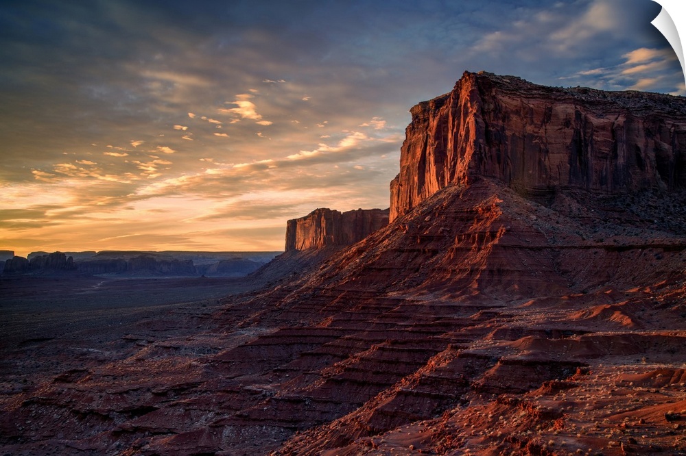The rising sun spreads warm light across the face of Monument Valley's Mitchell Mesa.