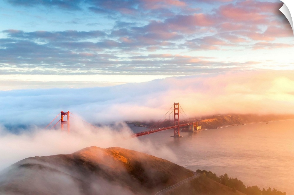 Aerial view of the Golden Gate Bridge surrounded by fog with the sunset coming in from the right.