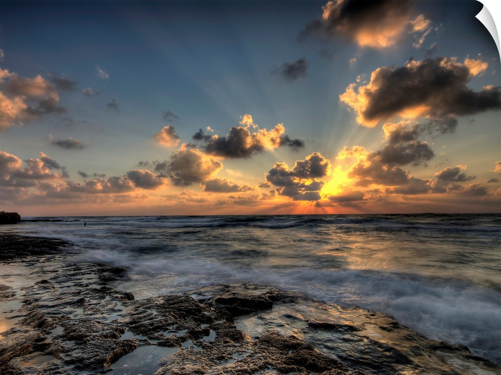 Horizontal photograph of a vibrant, golden sunset at a rocky beach.