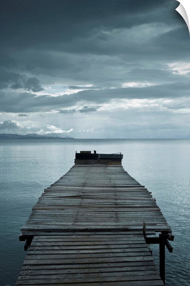 Photograph of a weathered dock over calm water with dark clouds overhead.