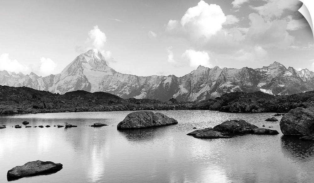 Black and white landscape image of a lake with snow covered mountains in the background.