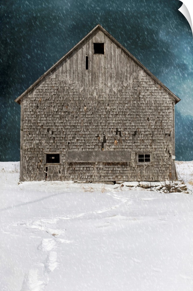 An old abandoned barn in a winter snow storm with footprints.
