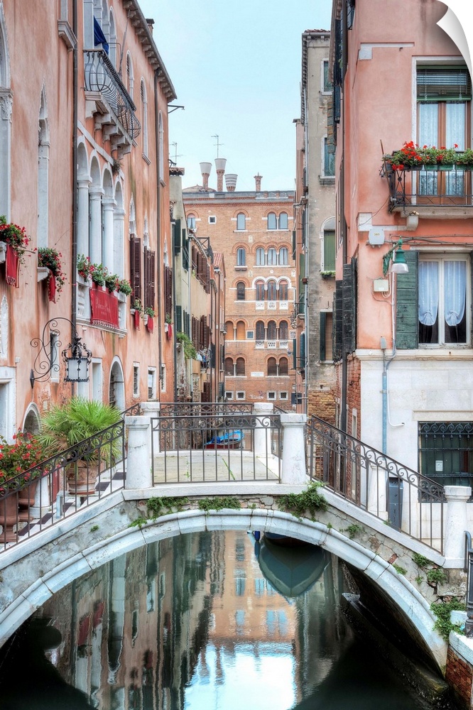 A vertical scene of a walking bridge over a canal with the city reflecting in the water in Venice, Italy.