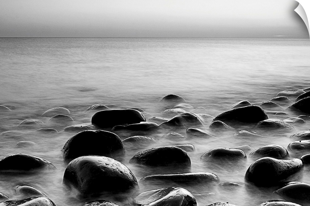 Black and white photograph of layers of smooth rocks covered by water.