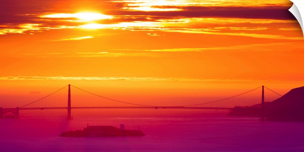 A photograph of a vibrant sky at sunrise, with a bridge in hazy, misty morning light.