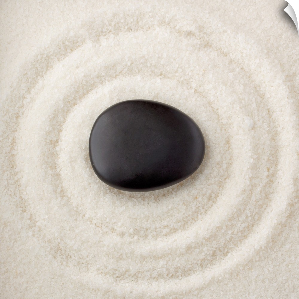 A smooth black rock in the middle of multiple rings in the sand.