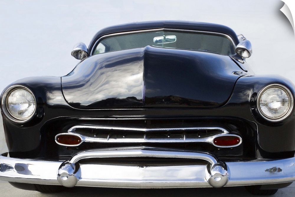 The front of a classic car with a chrome bumper and dark paint.