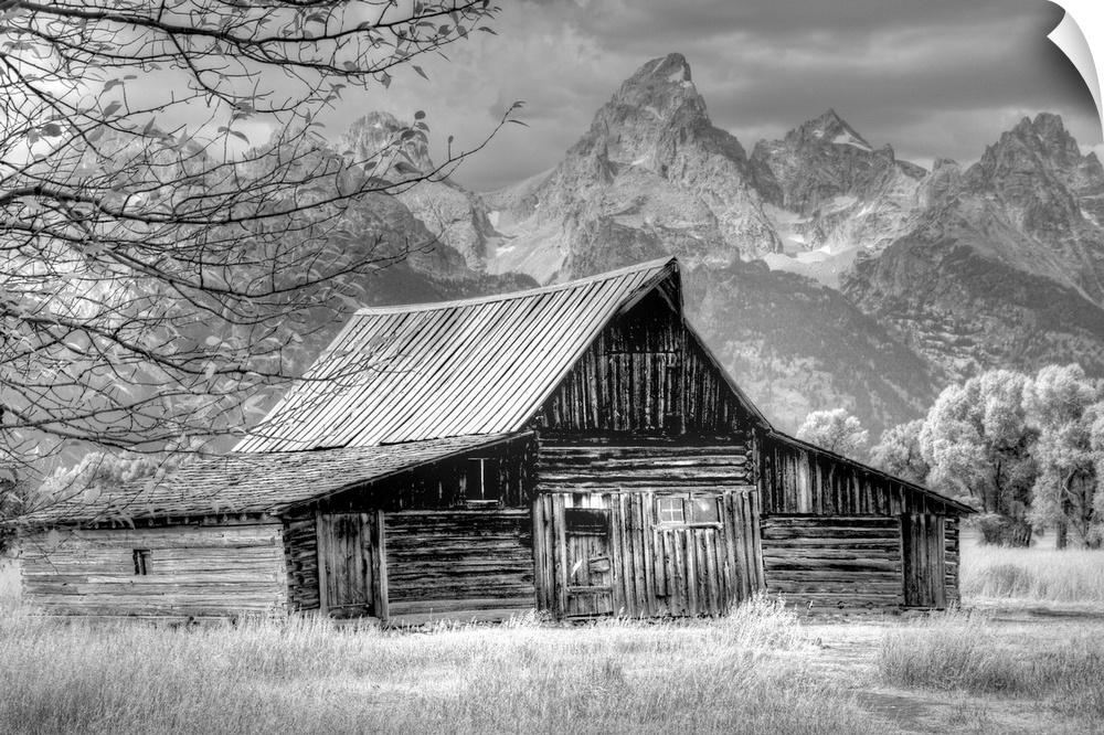 Black and white photo of an old barn in a field with the Grand Teton mountain range in the distance.