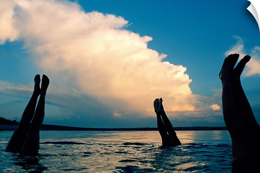 Three pairs of legs stick out of the water in Lake McConaughy, as a thunderstorm creeps forward in the distance.