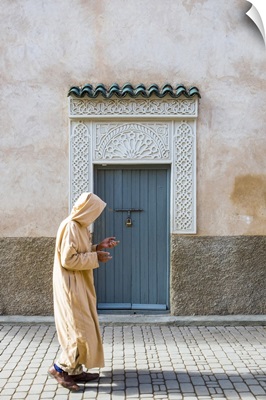 A man wearing a djellaba walks past a decorative doorway in the medina (old town)