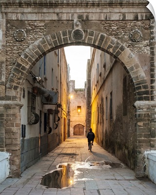 A person rides a bicycle through a dark alley in the medina old town at dawn