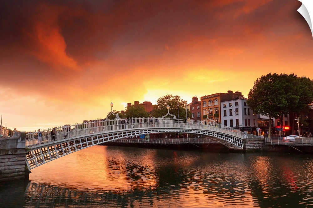 Europe, Dublin, Ireland, people crossing Halfpenny bridge on the Liffey river at sunset