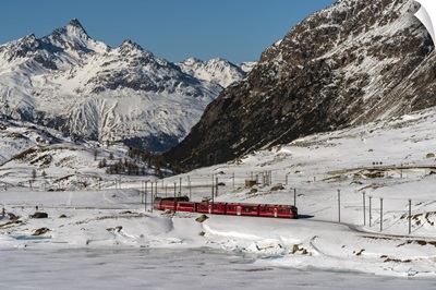 Famous Bernina Express red train passing Lago Bianco in a scenic winter landscape