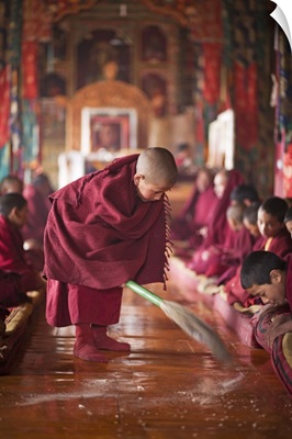 India, Ladakh, Thiksey, novice monk sweeping up the tsampa crumbs at morning prayers