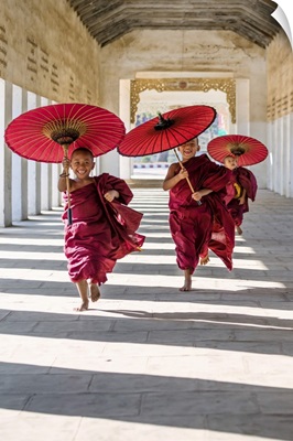 Myanmar, Mandalay division, Bagan. Three novice monks running with red umbrellas
