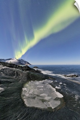 The Northern Lights illuminates the rocky peaks and icy sea in the polar night