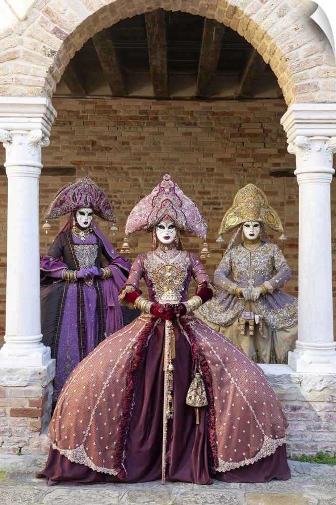 Three women wearing Indian style costumes and masks pose in the cloisters of Chiesa di San Francesco della Vigna, Venice, ...