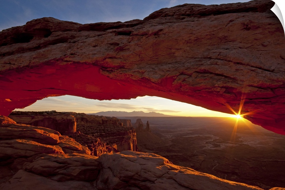 A photograph is taken through the mesa arch as the sun begins to rise over the horizon.