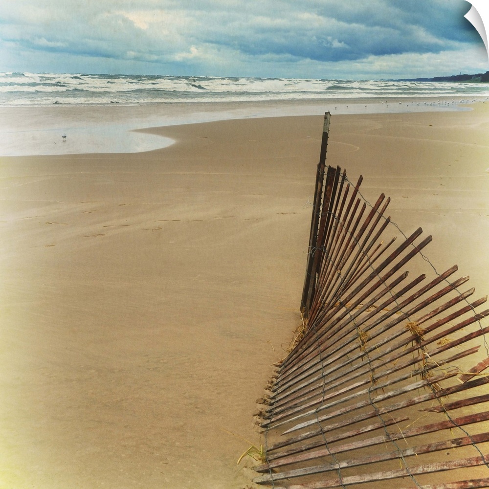 A worn down wooden fence on a sandy beach at low tide.