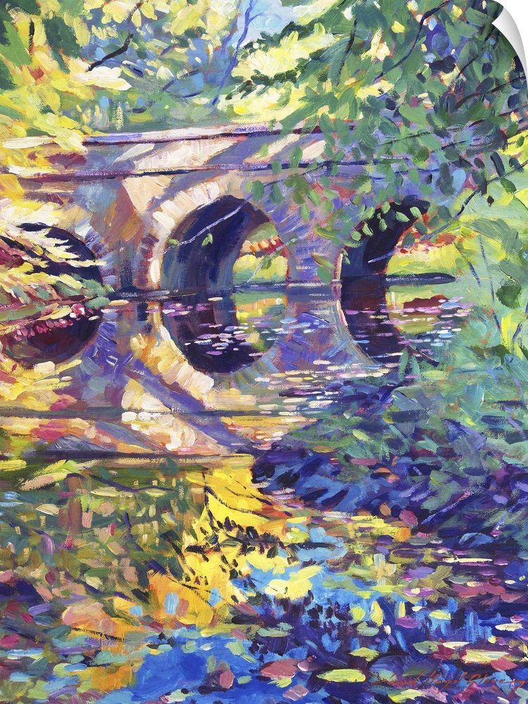 A stone bridge in a park over a colorful pond.