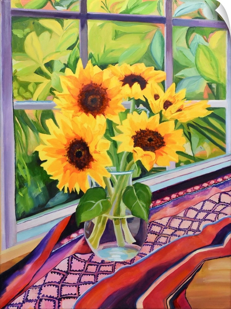 Sunflowers in glass vase on table with plants visible through window.