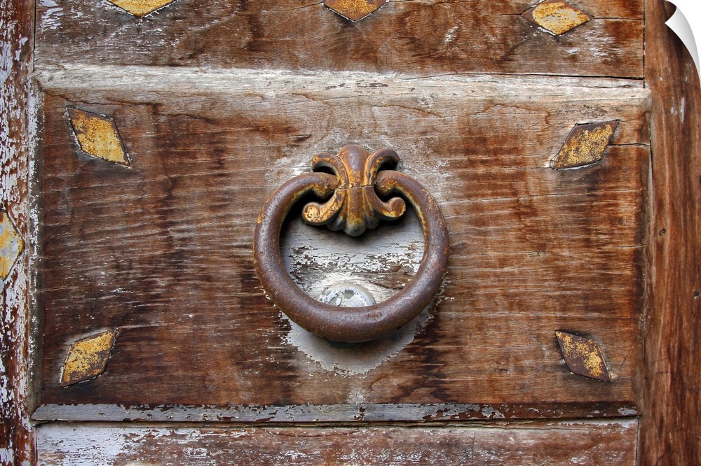 Photograph taken of an ornate door knocker. The door has faded over time and white paint has chipped off.
