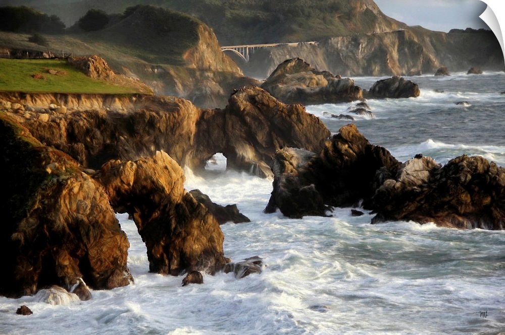 A spectacular view of the rugged coastline in Big Sur with the Rocky Creek Bridge in the distance. Two giant arches in the...