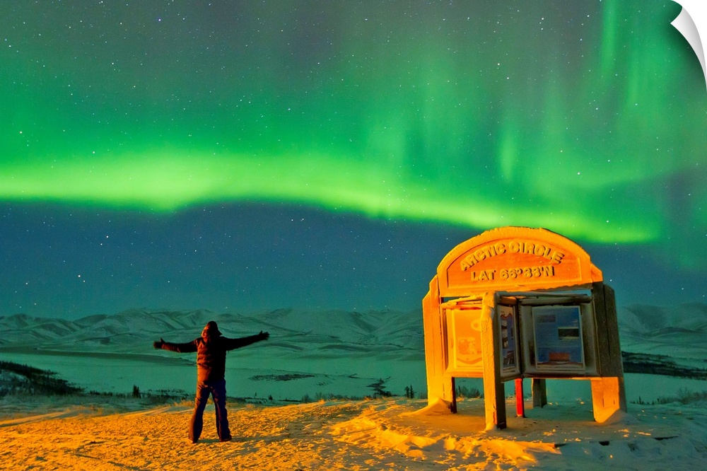 A man looks in awe at the northern lights near the Arctic Circle sign.